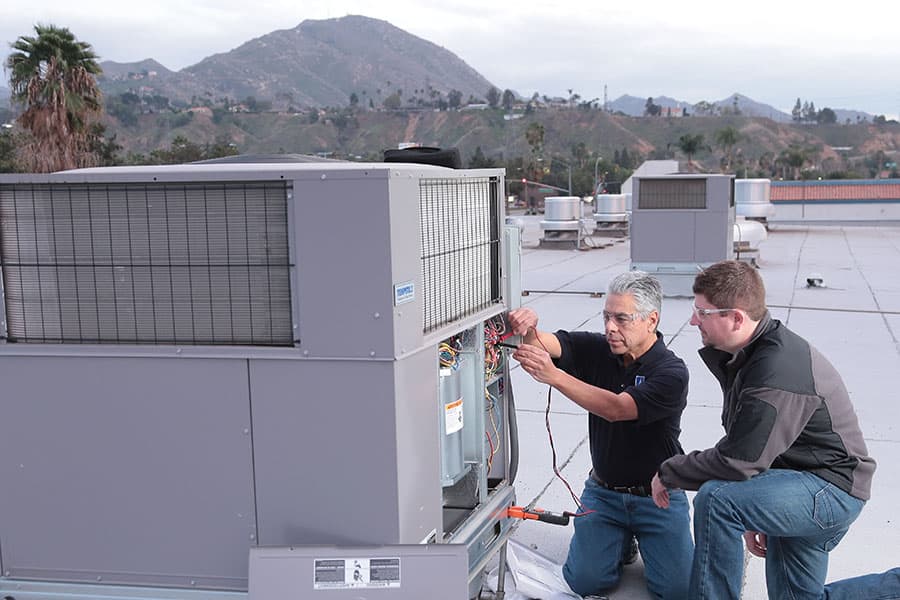 An HVAC student and instructor on a commercial rooftop in southern California, repairing a commercial air conditioner.