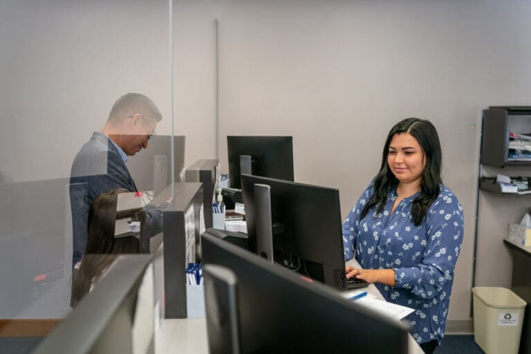 female billing coder at desk behind glass helping patient