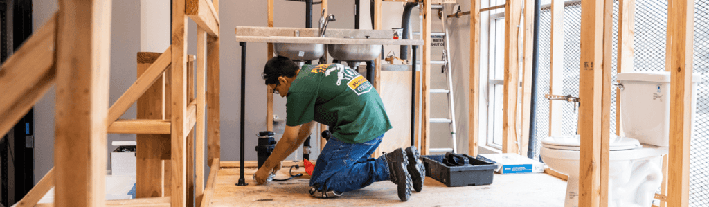 man in green t-shirt working on plumbing fixture